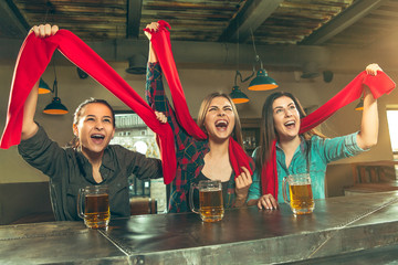 Sport, people, leisure, friendship, entertainment concept - happy female football fans or good young friends drinking beer, celebrating victory at bar or pub. Human positive emotions concept