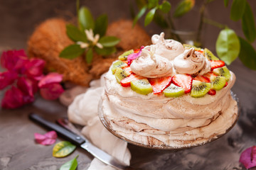 ropical aquafaba cake with kiwi, strawberry and coconut cream on dark table with ingredients and flowers