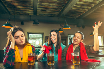 Sport, people, leisure, friendship, entertainment concept - happy female football fans or good young friends drinking beer, celebrating victory at bar or pub. Human positive emotions concept