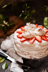 ropical aquafaba cake with strawberry and coconut cream on dark table with ingredients and flowers