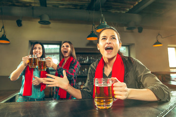 Sport, people, leisure, friendship, entertainment concept - happy female football fans or good young friends drinking beer, celebrating victory at bar or pub. Human positive emotions concept