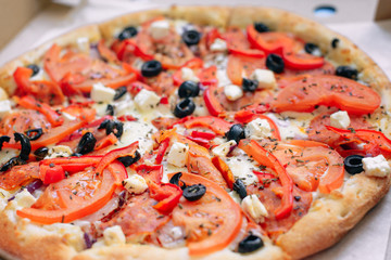 One Greek pizza in a cardboard box on a light background. The view from the top. Pizza delivery. Pizza menu. Pizza on the kitchen table.