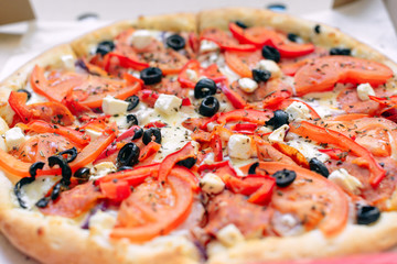 One Greek pizza in a cardboard box on a light background. The view from the top. Pizza delivery. Pizza menu. Pizza on the kitchen table.