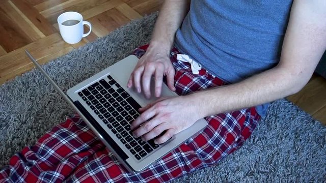 Closeup hands of young Caucasian man working on a laptop and drinking coffee