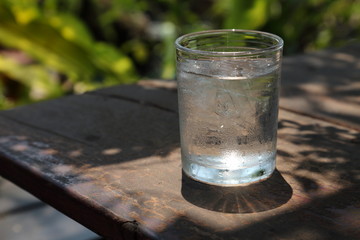 Cool glass of water with droplet on rustic wooden table with strong light