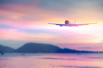 Fototapeta na wymiar Airplane flying over blur tropical beach with smooth wave and sunset sky abstract background.