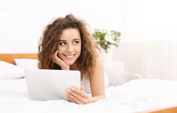 Cheerful young woman lying in bed with tablet