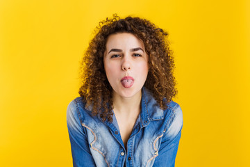 Beautiful curly girl showing tongue on a yellow background