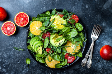 Citrus salad with mixed greens and blood orange on black ceramic plate. Vegan, vegetarian, clean eating, dieting, food concept. Dark stone background.