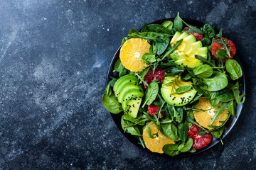 Citrus salad with mixed greens and blood orange on black ceramic plate. Vegan, vegetarian, clean eating, dieting, food concept. Dark stone background.