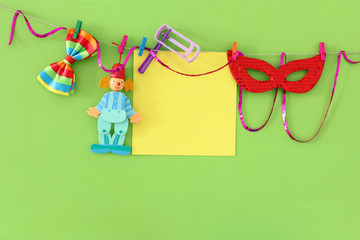 Purim celebration concept (jewish carnival holiday) with empty note for text, clown, mask and noisemaker over wooden green background