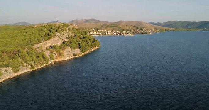 Village on croatian coast, C4k aerial, drone shot, parallel to the mediterranean shore and above the adriatic sea, towards the Zaboric town, near Sibenik, on a sunny, summer evening, in Croatia