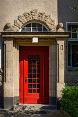 Verziertes Hausportal mit roter Türe in der denkmalgeschützten Wohnanlage Nonnendamm-Nord in Berlin-Siemensstadt