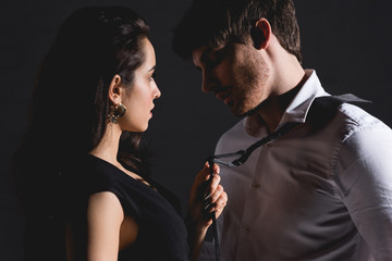man in white shirt and woman in dress standing and looking to each other isolated on black