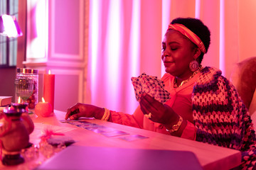 African american plump fortune-teller in ethnic adornments looking at the cards on the table