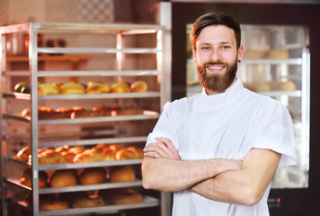 Young handsome male baker in white uniform against a background of baking and bread.