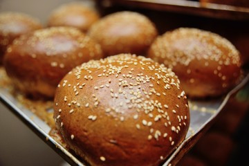 fresh appetizing buns with sesame seeds on a metal baking sheet close-up in the process of baking