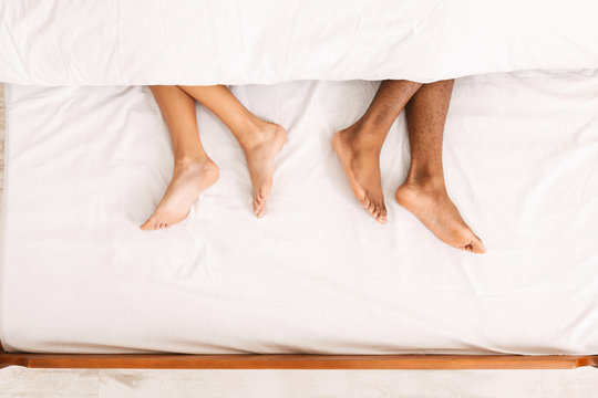Male and female legs under duvet lying on bed