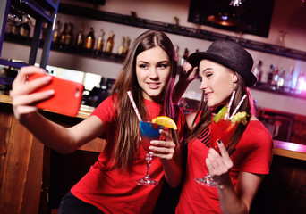 Obraz na płótnie Canvas selfie time. two cute young girlfriends drink cocktails and are photographed on a smartphone camera on the background of a bar in a nightclub