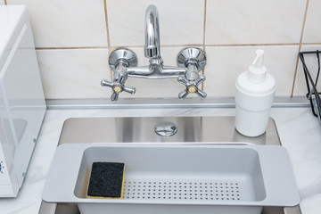 Modern kitchen sink and faucet, plastic sponge drying rack and dish washing liquid bottle.