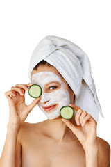 Beautiful young woman with facial mask on her face holding slices of cucumber. Skin care and treatment, spa, natural beauty and cosmetology concept, isolated over white background