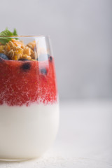 Glass of yogurt with strawberry mousse, blueberries and granola on a white background