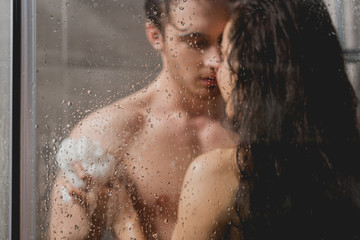 selective focus of man and beautiful woman hugging and taking shower with loofah in cabin