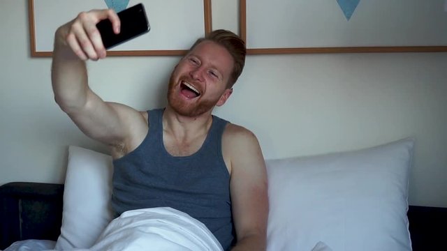 Young Ginger Man taking selfies in bed