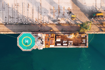 Scenic aerial view of moored cargo ship with helicopter landing pad in city seaport. Dark sea...