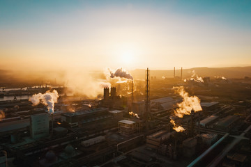 Fototapeta premium Aerial view, the vast territory of a large industrial chemical plant with high pipes in the bright light of winter sunset. Thick smoke comes from a high pipe. Environmental pollution. Drone