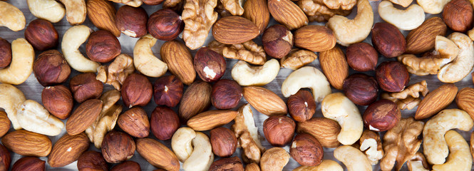 Mixed nuts (cashew, hazelnuts, walnuts, almonds) on white wooden surface, top view. From above, overhead.