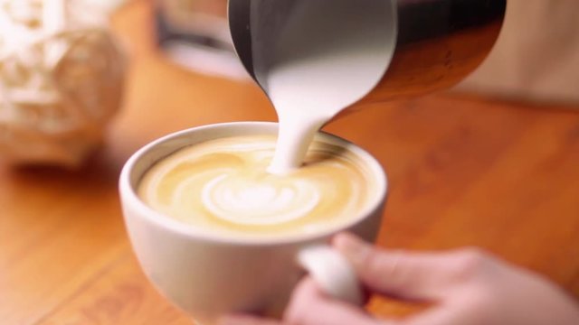Barista draws milk over a coffee - making latte art for cappuccino. Barista making of cafe latte art, heart shape.