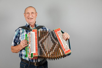 Portrait of a man, grandfather plays the accordion. On a gray background