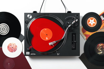 Top view of a turntable with red heart-shaped vinyl record a stylus with a needle, on white...