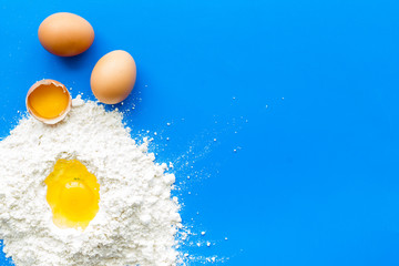 Baking background with eggs and flour on blue table. Top view.