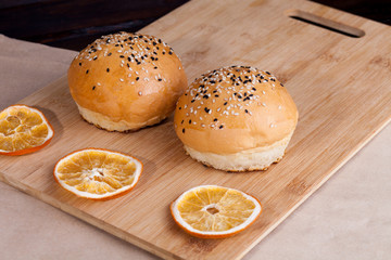 Hot sweet buns on a rustic background. Shaped food with sesame on cutting board around with dry oranges