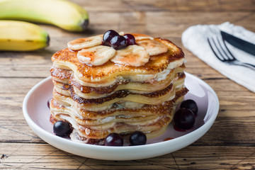 Pancake cake with bananas and berry syrup, selective focus, dark background.