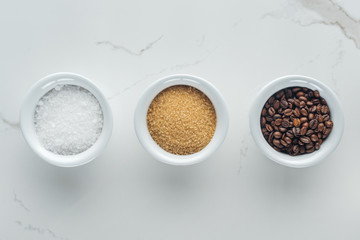 top view of bowls with salt, coffee grains and brown sugar on white surface