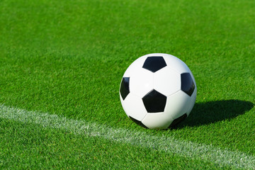 A classic soccer ball lies on the bright green grass on the football field in the designated area of the penalty area at a sports stadium close-up in a large sports center for football players