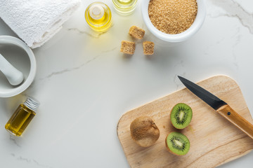 Obraz na płótnie Canvas top view of wooden cutting desk with cut kiwi, surrounded by different cosmetic components on white surface