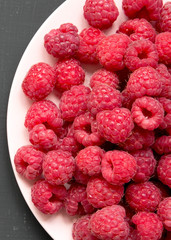 Raspberry on a pink plate on black background, top view. Flat lay, overhead, from above. Close-up.