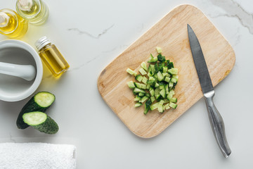 top with of wooden cutting desk with cut cucumber cubes, and various ingredients for cosmetics...