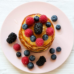 Top view, pancakes with berries and honey on a pink plate. Overhead, from above.