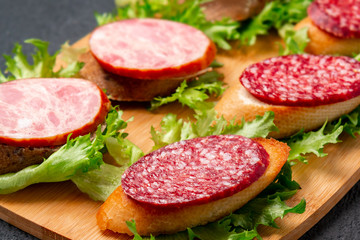 Several sandwiches with sausage and salami and sauce on a black board, background with copyspace