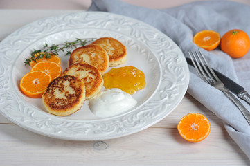 Cheesecakes with citrus jam and sour cream. Light wooden background. Close-up. The concept of delicious breakfast.