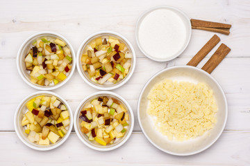 Uncooked chopped mixed fruits step. recipe step by step crumble with fruits in a ceramic ramekin flatlay on white wood