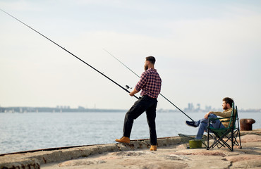 leisure and people concept - happy friends with fishing rods on pier at sea