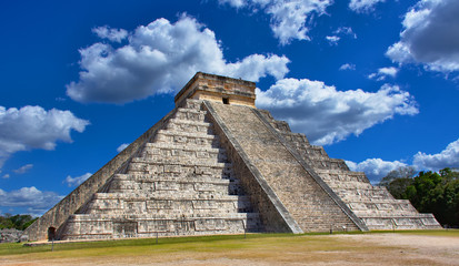 Fototapeta na wymiar Sunny day with blue sky and white clouds. No people around. El Castillo (The Kukulkan Temple) of Chichen Itza, mayan pyramid in Yucatan, Mexico - Mar 2, 2018
