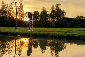 Healthy Sport. Asian Sporty woman golfer player chips and swing golf on the green sunset evening...