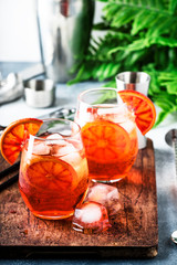 Aperol spritz cocktail in wine glass with sparkling wine, liqueur, ice cubes and red orange - summer Italian low alcohol cold drink, gray stone bar counter background with tools,  selective focus